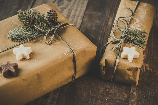 two gifts wrapped in brown wrapping paper with twine and white stars sitting on dark brown hardwood floor
